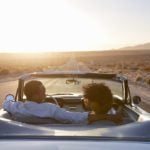 Rear view of an expat and expat spouse driving into the sunset in a classic convertible